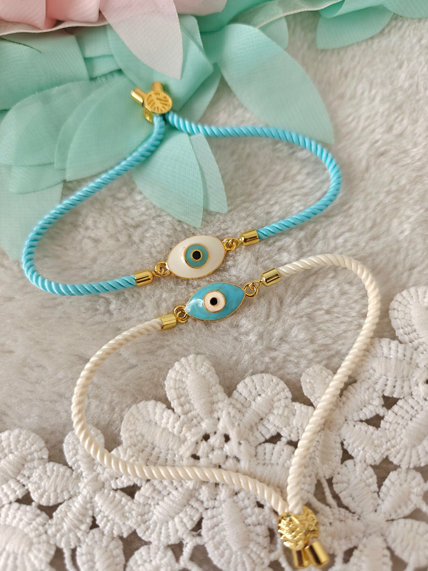 Evil eye bracelet rakhi with oval charm and adjustable rope threads in blue and white on soft background