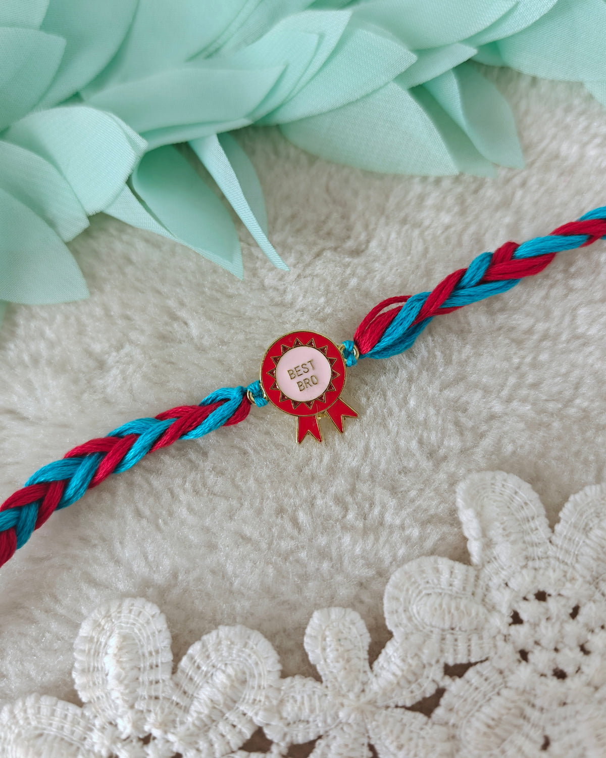 Best bro rakhi with badge charm and teal red braided threads on soft background