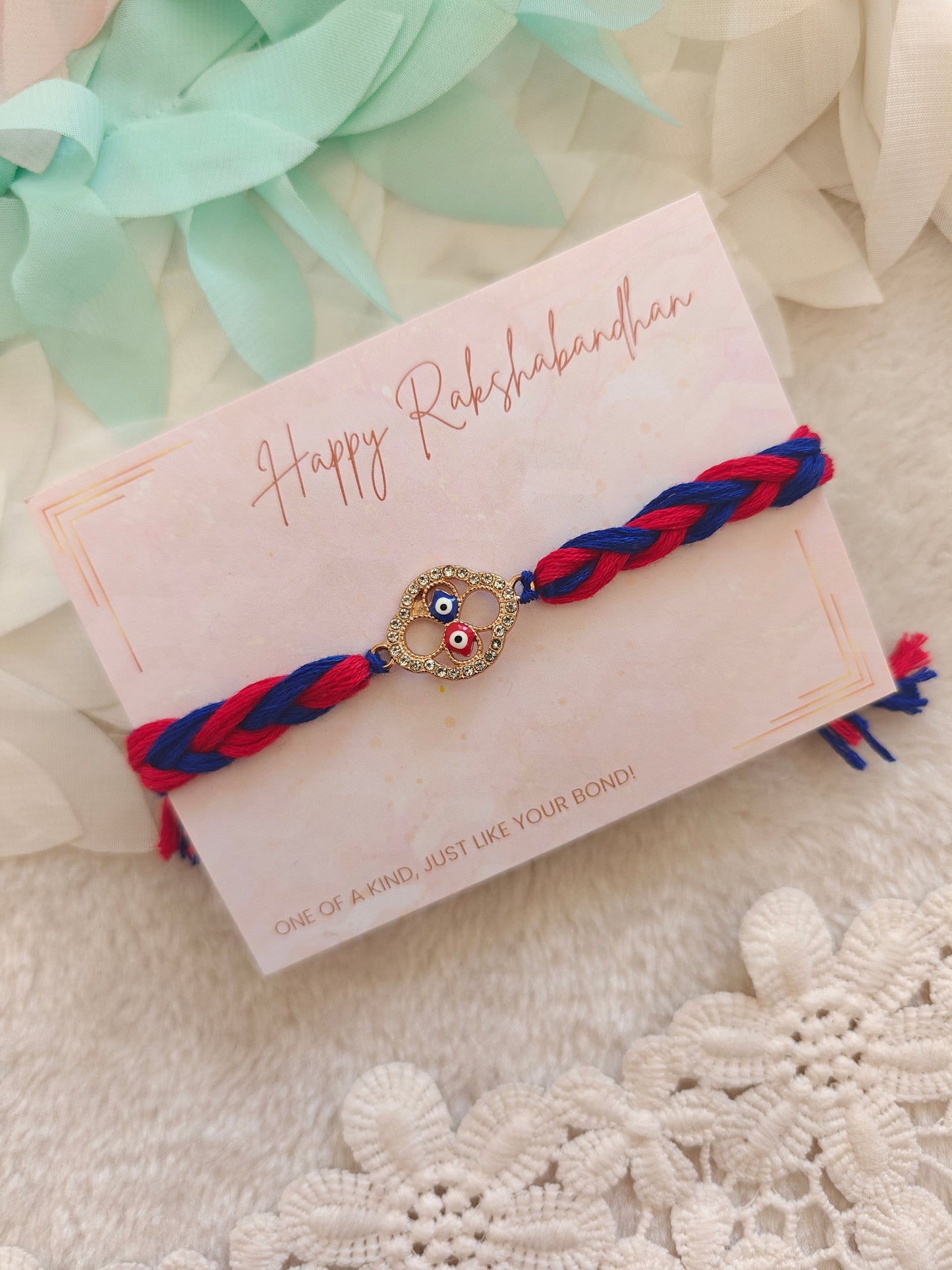 dual evil eye rakhi with red and blue braided thread and stone charm