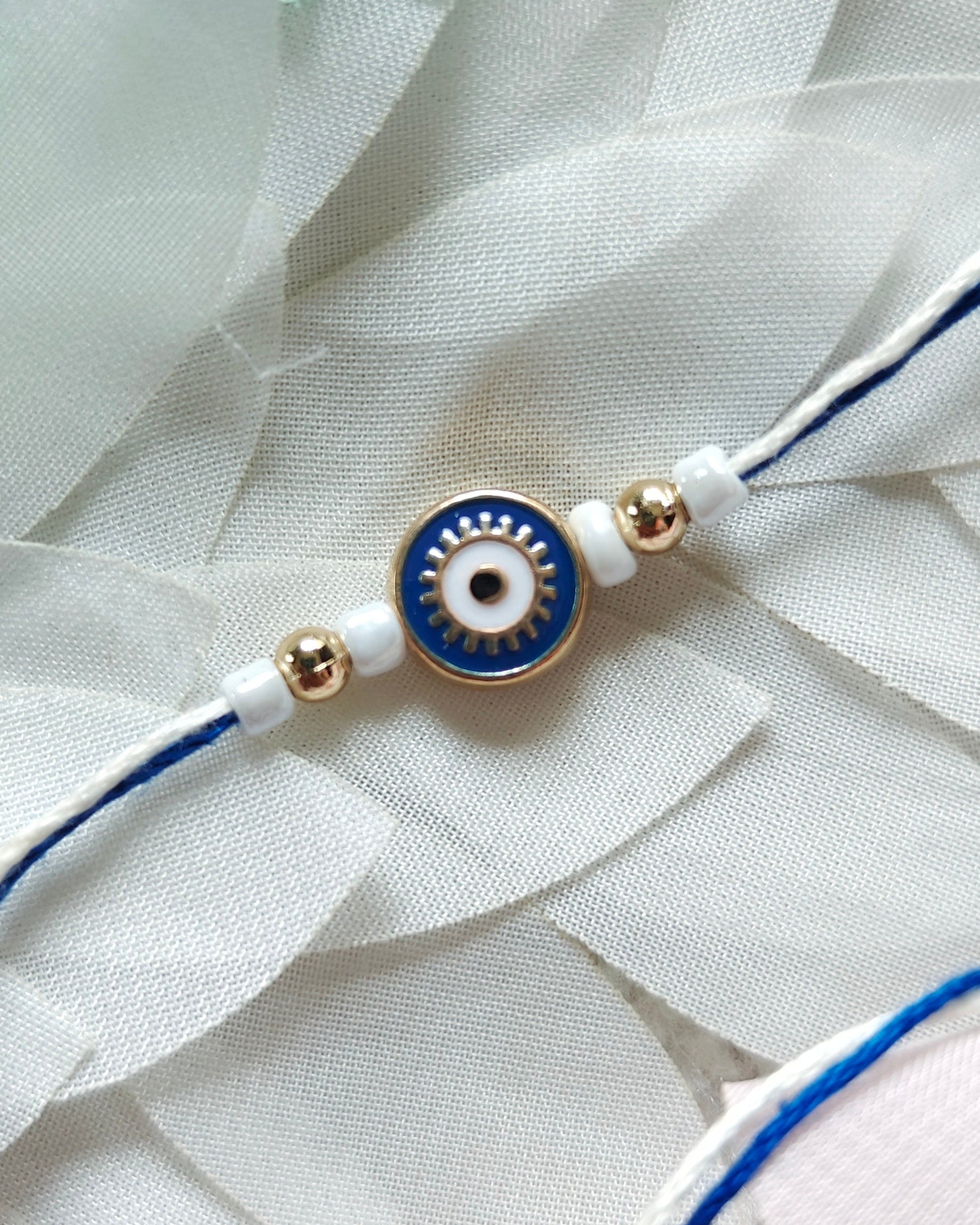 Blue evil eye rakhi with white beads and gold accents on minimal thread, handmade nazar rakhi for brother