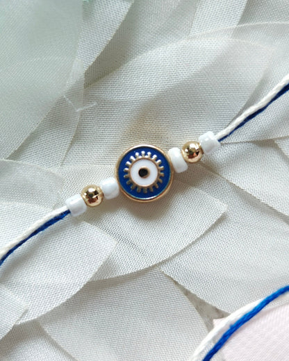 Blue evil eye rakhi with white beads and gold accents on minimal thread, handmade nazar rakhi for brother