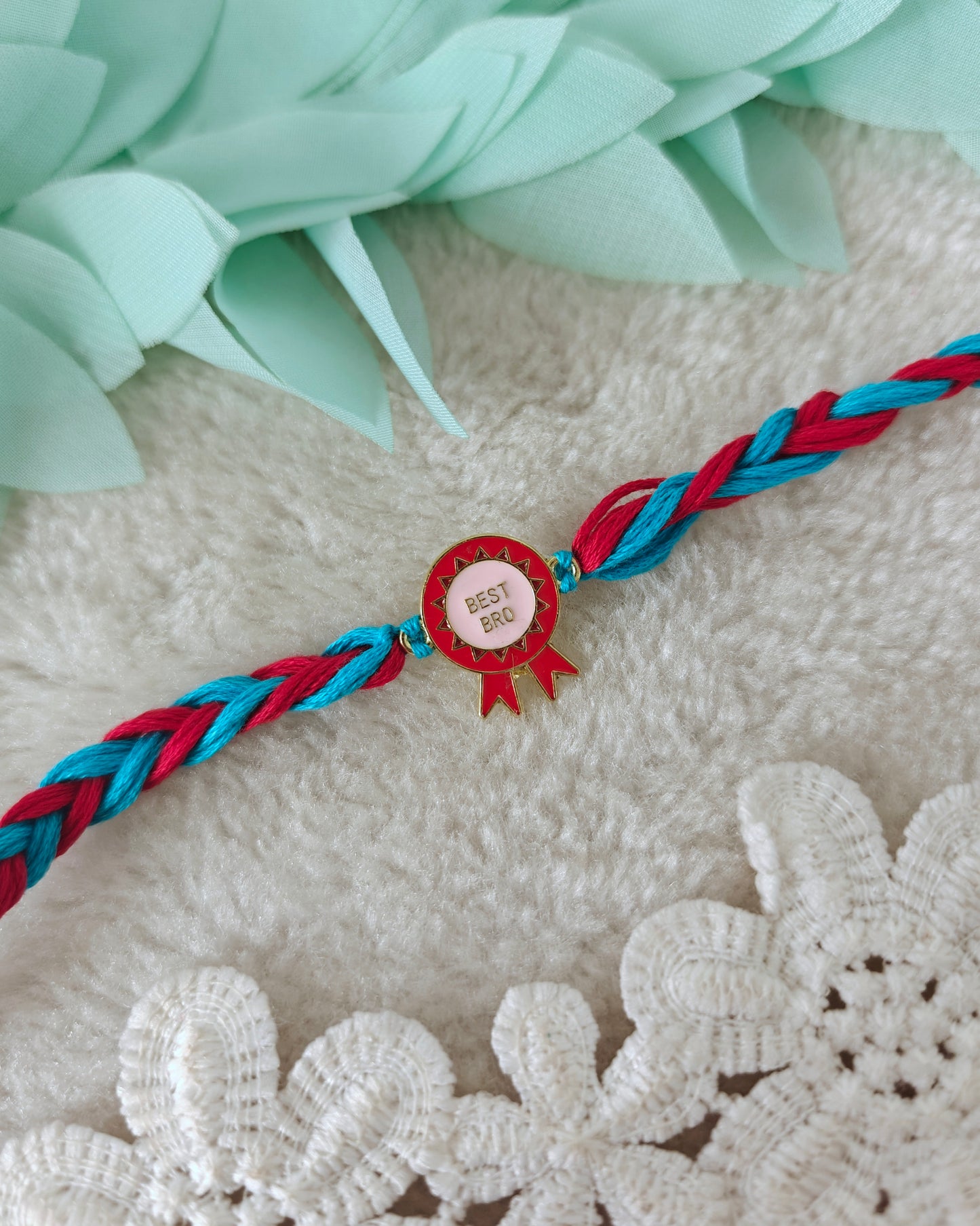 Best bro rakhi with badge charm and teal red braided threads on soft background