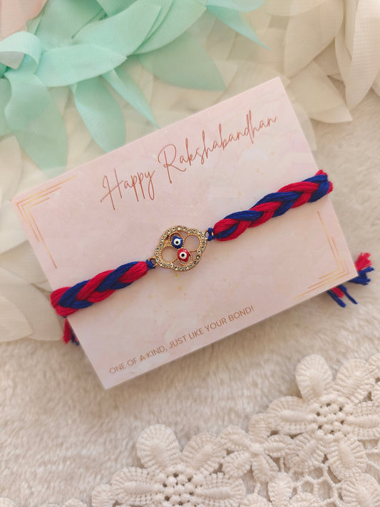 dual evil eye rakhi with red and blue braided thread and stone charm