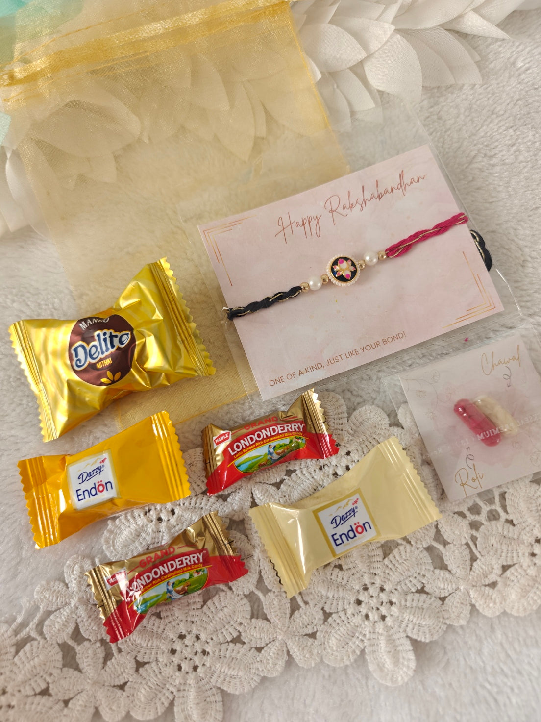 Designer rakhi hamper with assorted candies, roli chawal pack, and organza gift pouch for Raksha Bandhan.