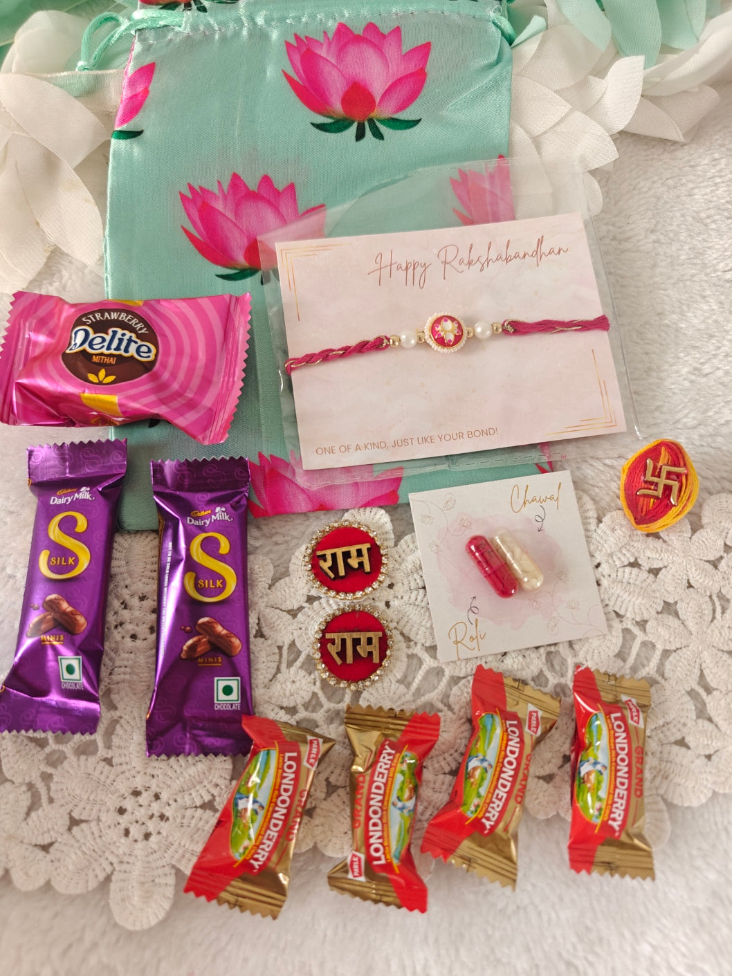Rakhi gift hamper with designer rakhi, Dairy Milk Silk chocolates, candies, roli chawal, Ram naam embellishments, and lotus print potli.